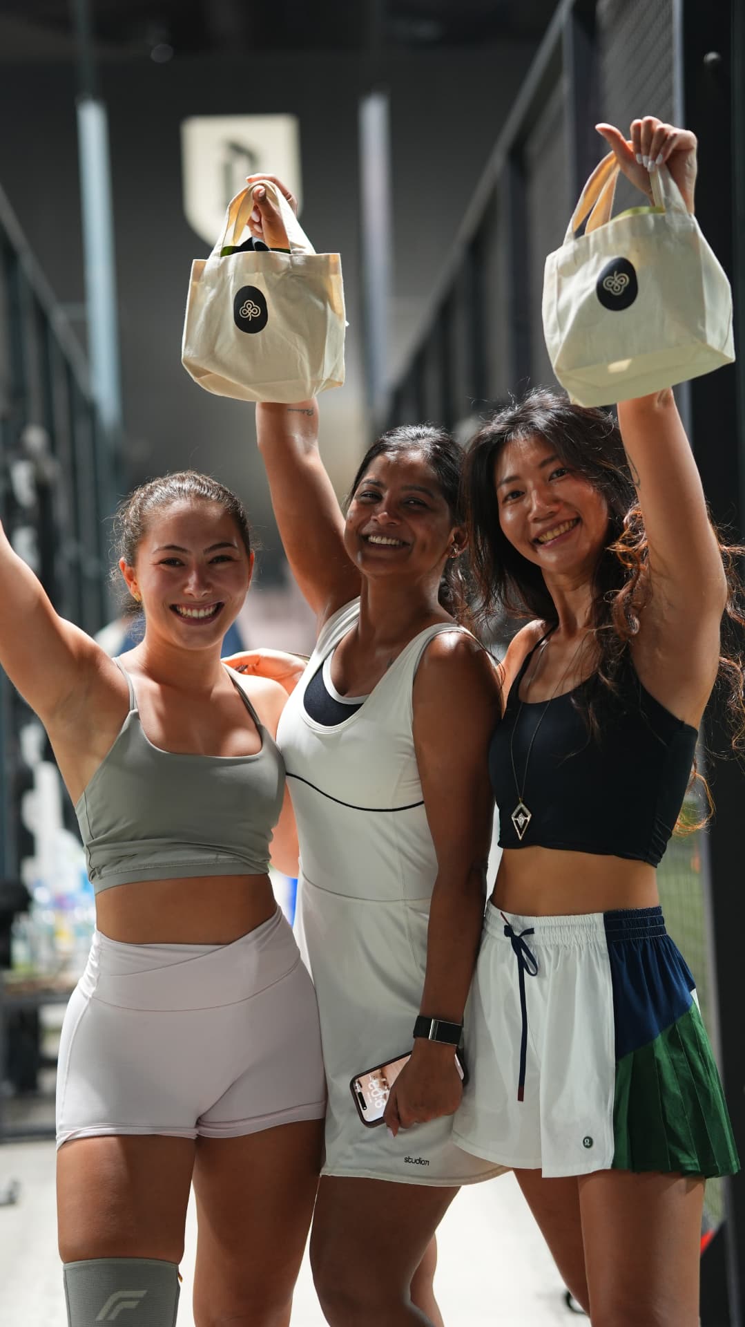 Three players posing playfully with their gift bags between the courts