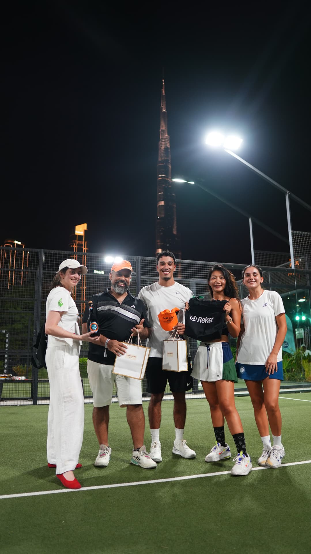 Players holding their prizes on court with the Burj Khalifa behind