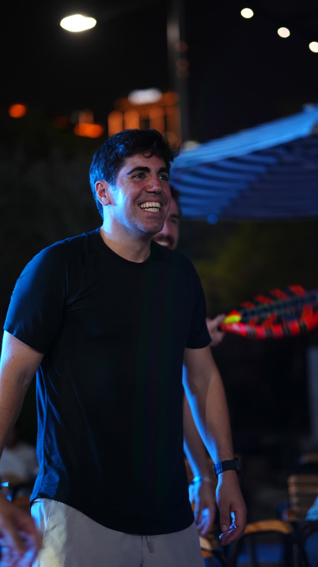 A guest smiling at night beside a padel racket