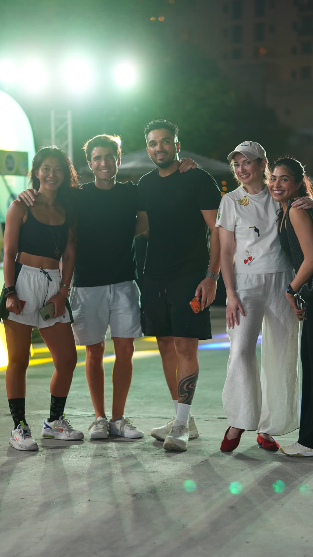 Five guests standing arm in arm and smiling under the court lights
